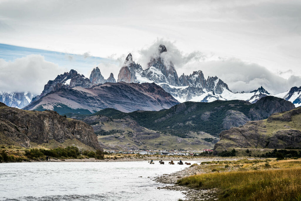 Horses crossing a river in the shadow huge snowcapped mountains in Patagonia on the Gaucho Derby ultra endurance horse race